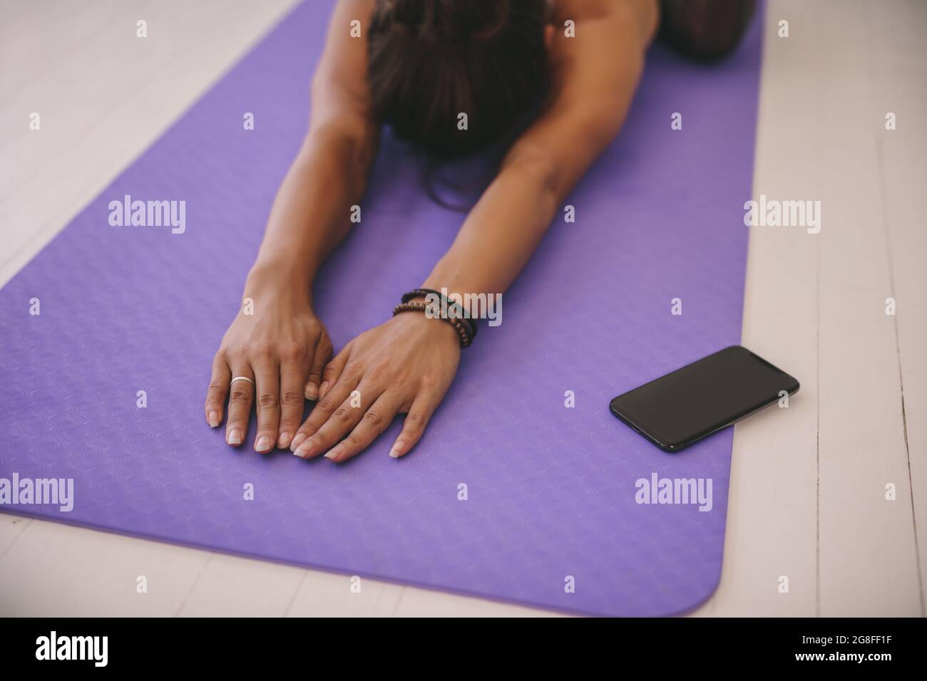 Donna che fa l'allenamento stretching sul tappetino per esercizi. Donna che fa il bambino posa yoga in palestra, con il fuoco sulle mani e lo smartphone davanti. Foto Stock