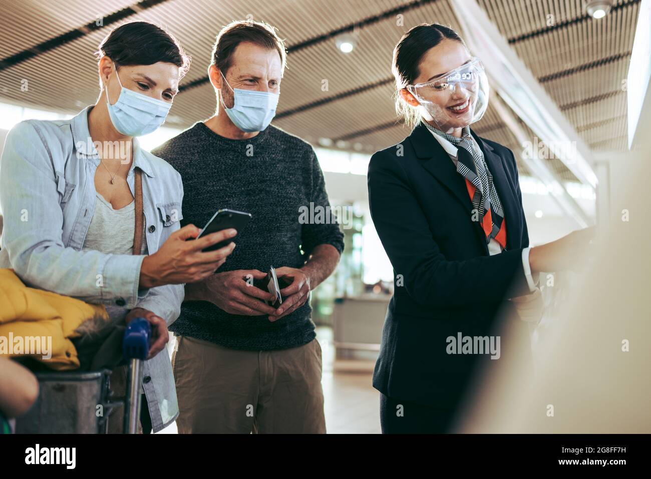 Il personale dell'aeroporto in scudo aiuta le coppie in maschere di protezione durante la pandemia. Turisti maschili e femminili in maschere di faccia aiutati da addetto di terra all'airpor Foto Stock