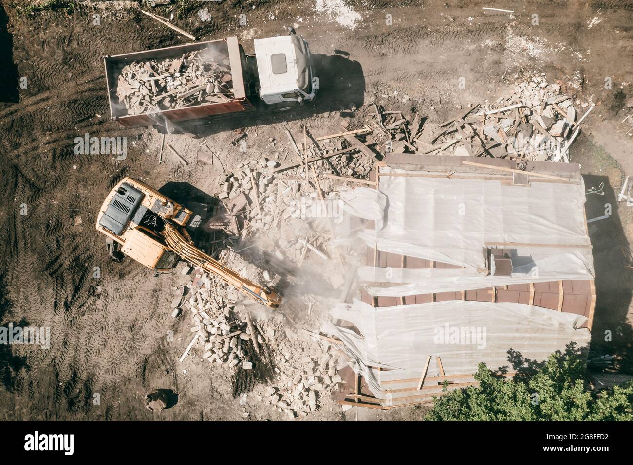 Escavatore con benna si rompe casa. Demolizione di edifici, vista dall'alto dal drone. Foto Stock