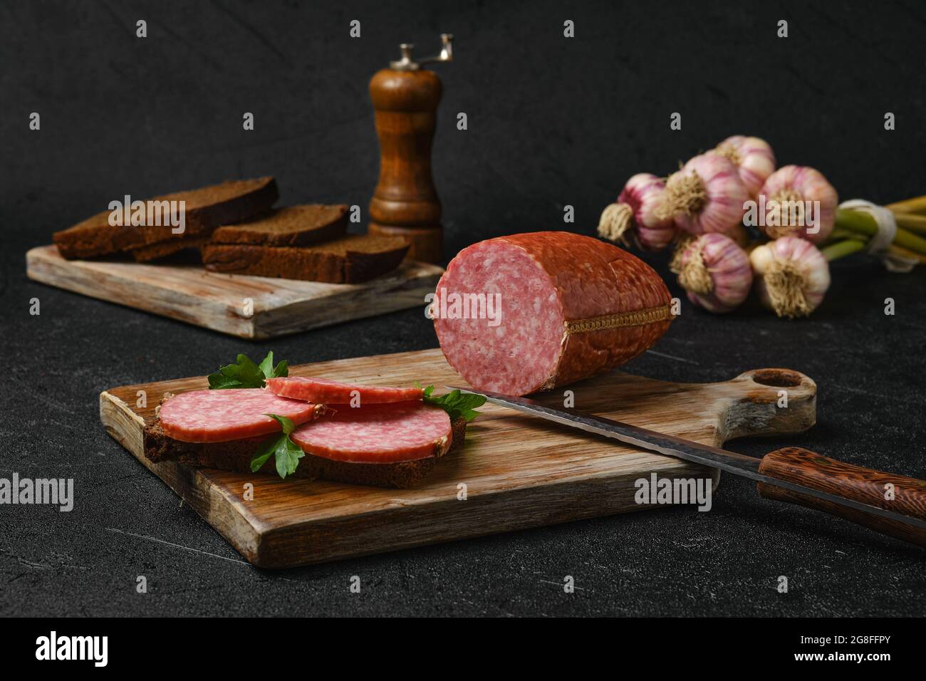 Salame di manzo affumicato e panino sul tagliere su sfondo nero Foto Stock