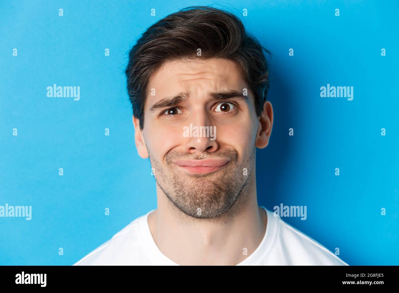 Colpo di testa di uomo scettico e deluso, grimacing complicato, in piedi su sfondo blu Foto Stock