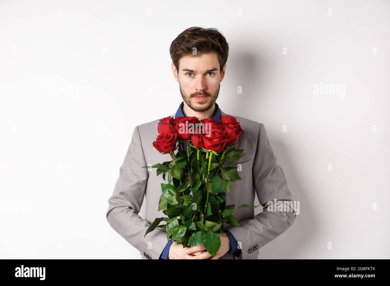 Concetto di giorno e amore di San Valentino. Uomo sicuro e bello in tuta  che tiene bouquet di rose, guardando la macchina fotografica, in piedi su  sfondo bianco Foto stock - Alamy