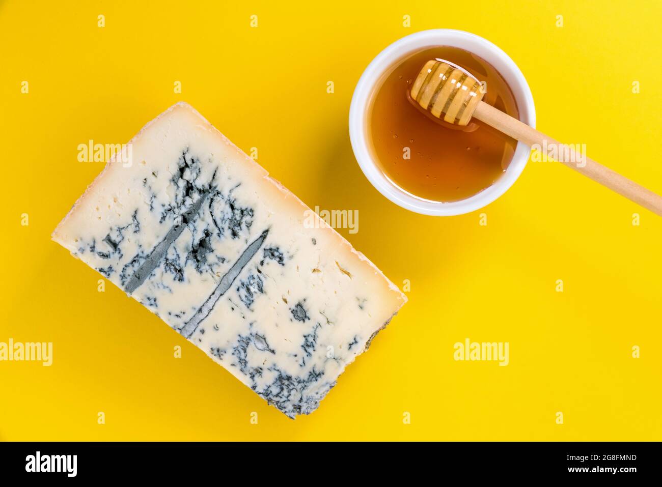Gorgonzola italiana, fetta di formaggio a muffa blu con ciotola al miele con cucchiaino di miele su sfondo giallo, vista dall'alto, piatto, spazio copia Foto Stock