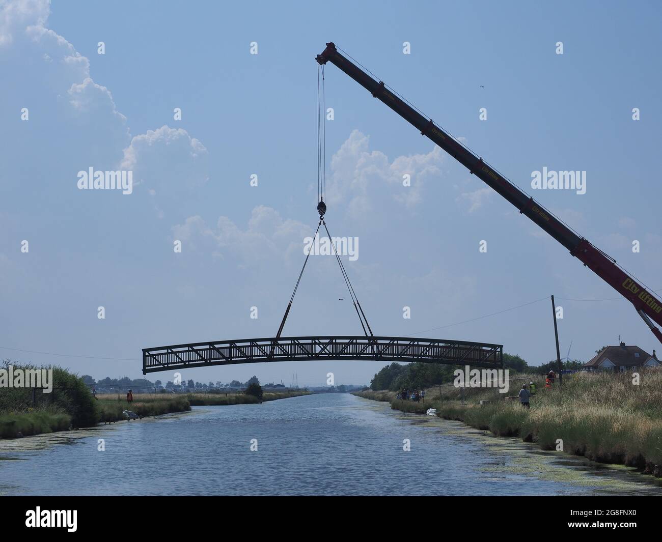 Sheerness, Kent, Regno Unito. 20 luglio 2021. Una grande gru ha sollevato un nuovo ponte a piedi in posizione questo pomeriggio attraverso lo storico canale difensivo Sheerness / Queenborough Lines risalente al 1868 (forma attuale) e prima (1667) proteggere cantiere navale Sheerness da attacchi di terra. Queenborough Lines è un Monumento programmato elencato di importanza nazionale; particolare attenzione ha dovuto essere presa con l'installazione, che ha richiesto 2 giorni. Le fondamenta sono state progettate per non disturbare il terreno. Il ponte pedonale/ciclabile fa parte della rete ciclistica nazionale di Sostrans. Credit: James Bell/Alamy Live News Foto Stock