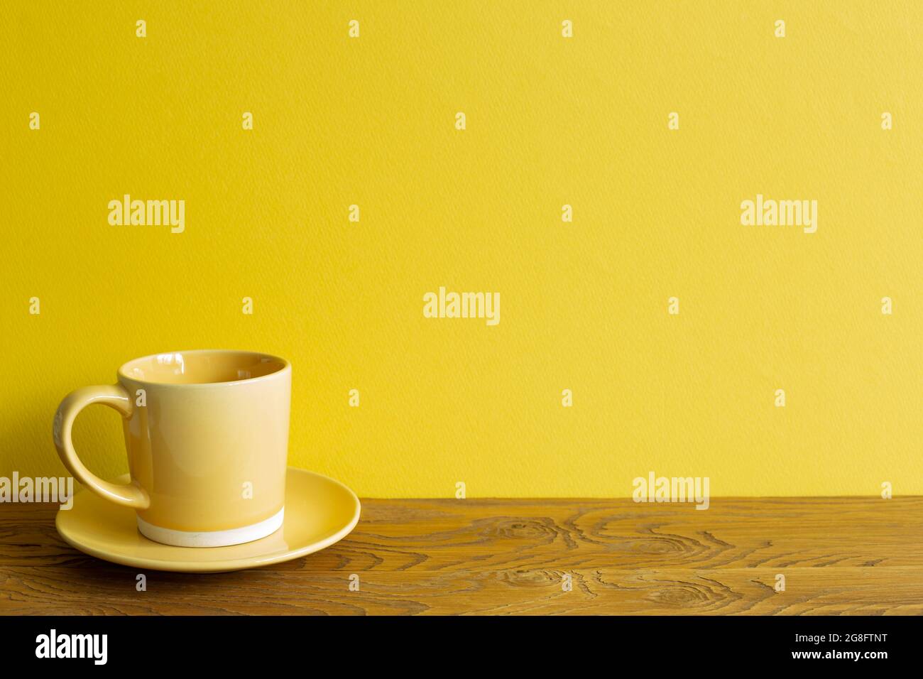 Tazza di caffè gialla su tavolo di legno. Sfondo giallo della parete. Spazio per la copia Foto Stock