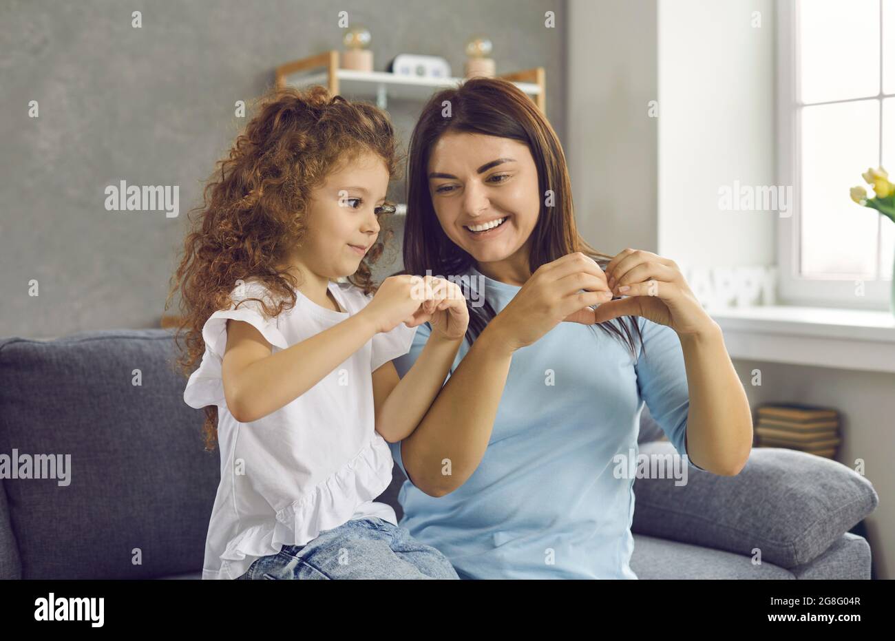 Madre felice e piccola figlia sorridenti l'una all'altra e facendo il gesto del cuore della mano Foto Stock