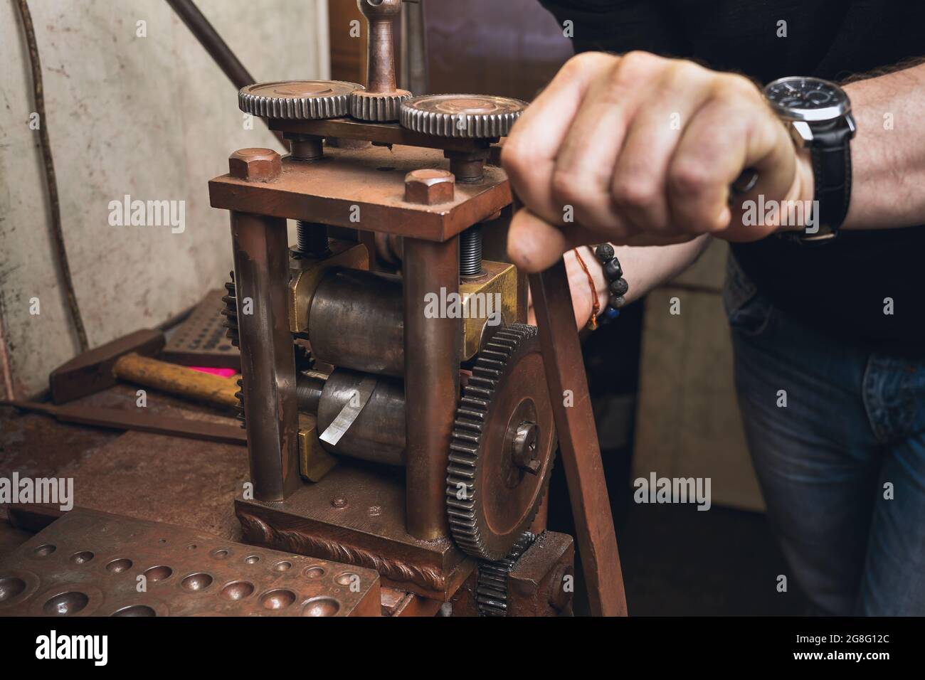 Un gioielliere rotola un foglio di metallo per l'uso nel suo lavoro Foto Stock