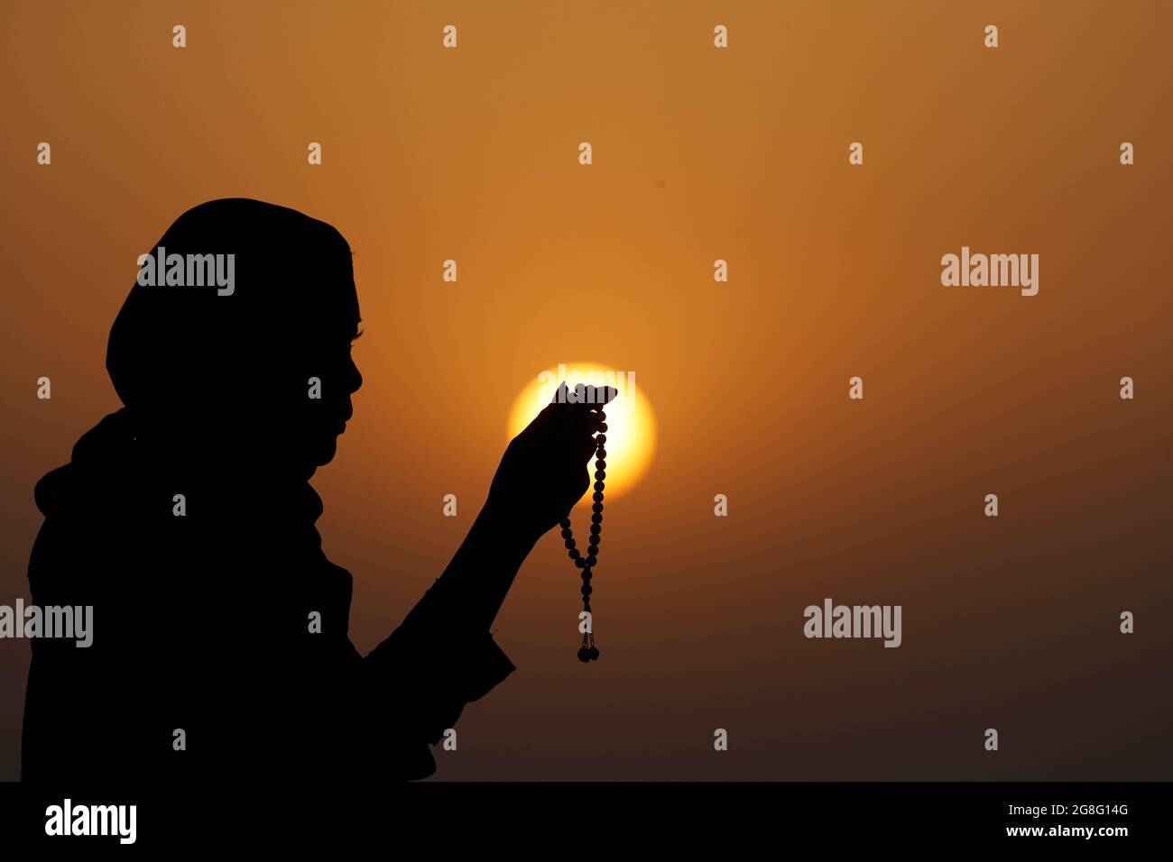 Silhouette di una donna musulmana che tiene in mano perline di preghiera e prega al tramonto, Emirati Arabi Uniti, Medio Oriente Foto Stock