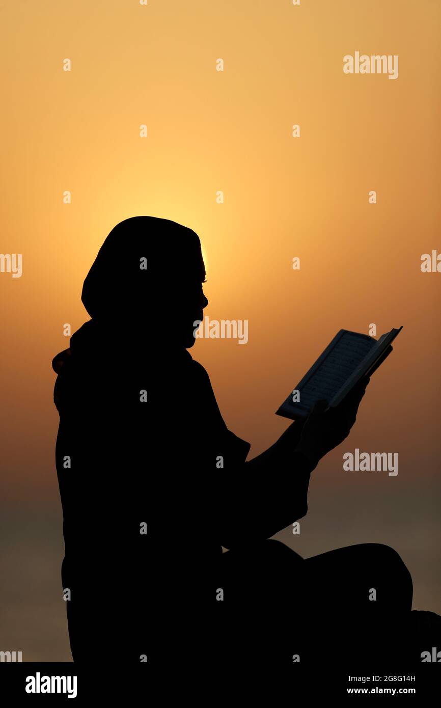 Silhouette di una donna musulmana che legge il Noble Quran al tramonto, Emirati Arabi Uniti, Medio Oriente Foto Stock