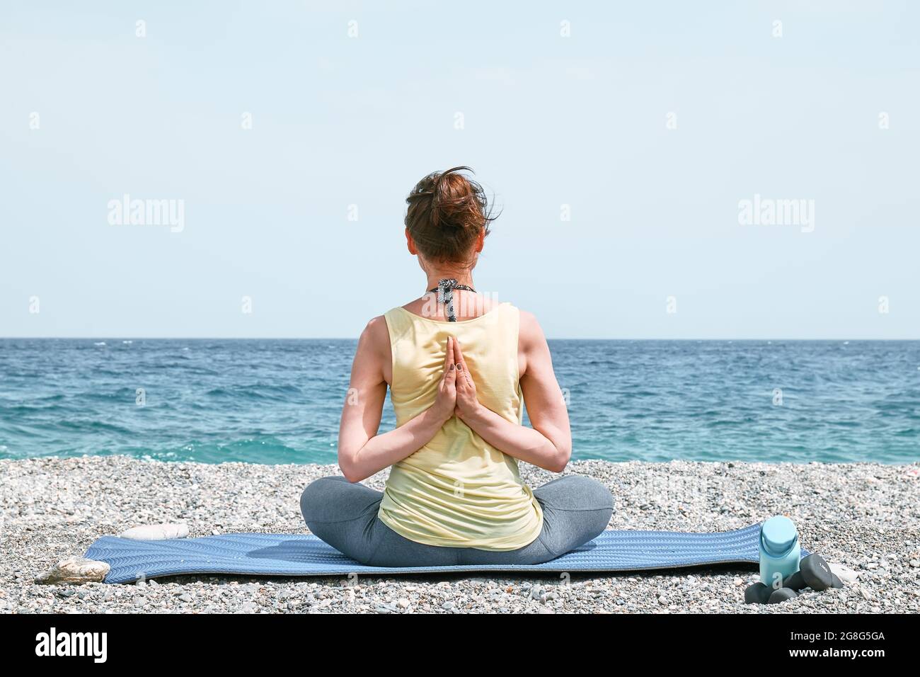 Donna snella che fa Gomukhasana o faccia di mucca posa sulla spiaggia al mattino. Rinforzare i muscoli delle gambe e coordinazione del corpo. Praticare lo yoga Foto Stock