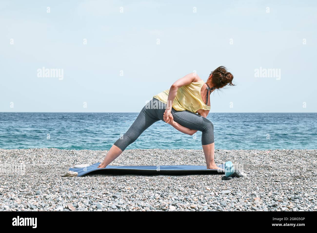 Slim Woman facendo Baddha Parsvokonasana o Bound Side angolo posa sulla spiaggia al mattino. Rinforzare i muscoli delle gambe e coordinazione del corpo. P. Foto Stock