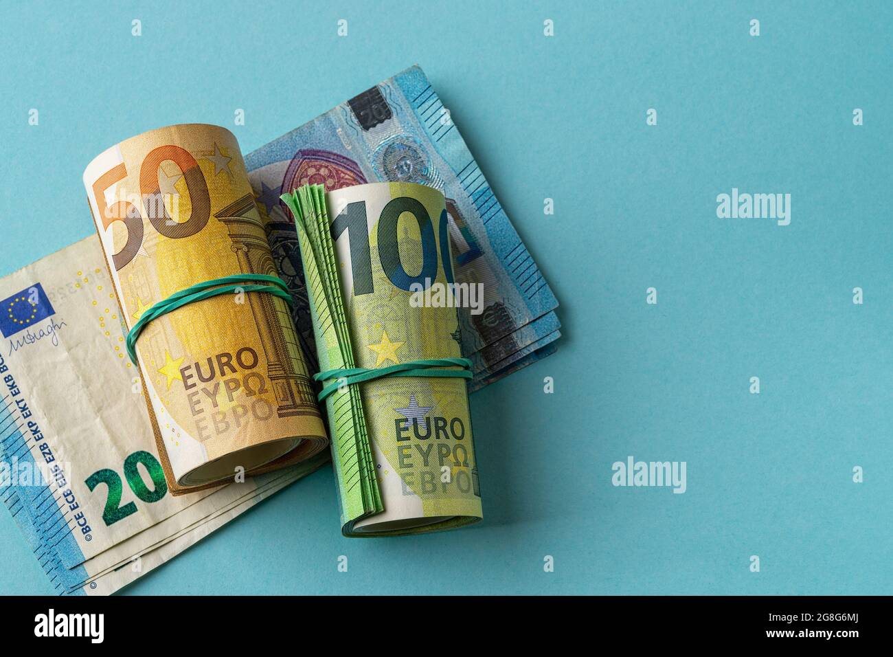 Rotolo verde di banconote da 100 euro e rotolo arancione di banconote da 50  euro oltre 20 euro di carta moneta su sfondo blu. Reddito, spese e  risparmio in contanti Foto stock - Alamy