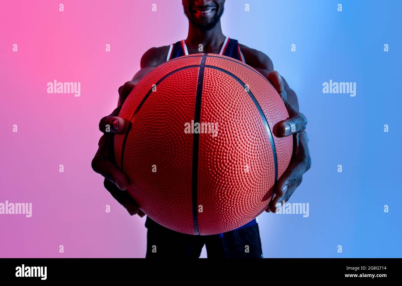 Sportivo nero irriconoscibile che tiene il basket in mani distese con luce al neon e messa a fuoco selettiva Foto Stock