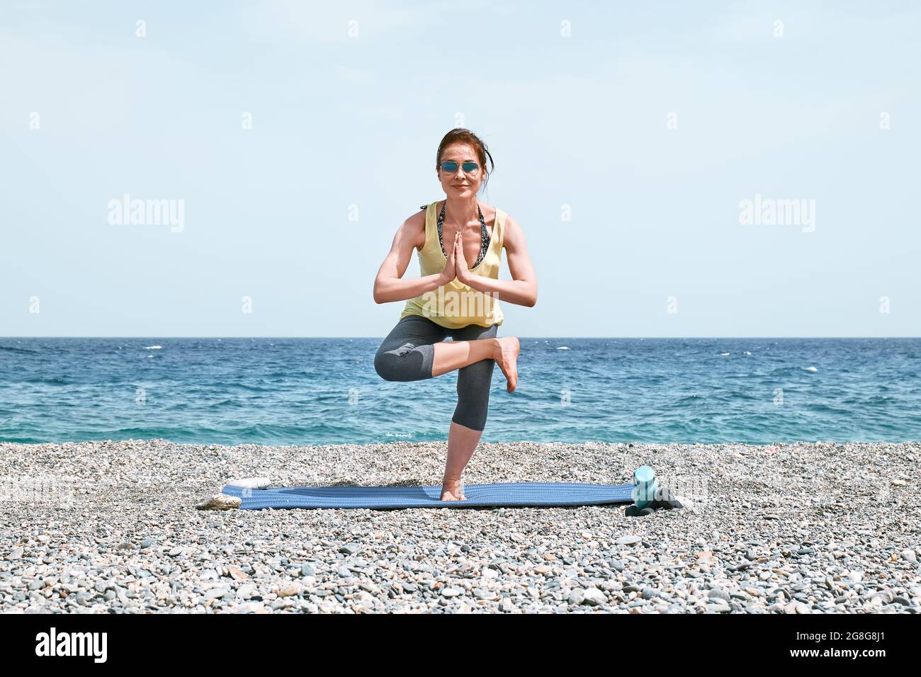 Donna snella che fa Virksasana o posa albero sulla spiaggia al mattino. Rinforzare i muscoli delle gambe e coordinazione del corpo. Praticare yoga all'aperto Foto Stock