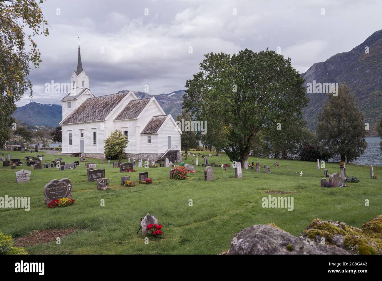 Tradizionale chiesa cristiana in legno bianco in stile scandinavo con cimitero intorno ad essa. Giorno nuvoloso nella campagna norvegese. Foto Stock