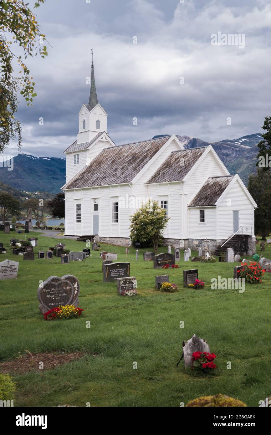 Immagine verticale di una tradizionale chiesa cristiana in legno bianco in stile scandinavo con cimitero intorno ad essa. Giorno nuvoloso nella campagna norvegese. Foto Stock
