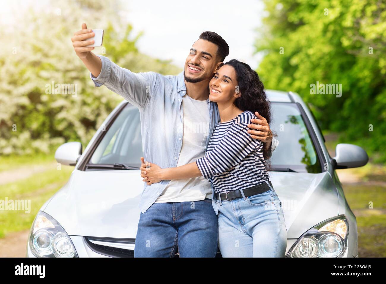 Coppia di gara mista amorevole in piedi in auto, prendendo selfie Foto Stock