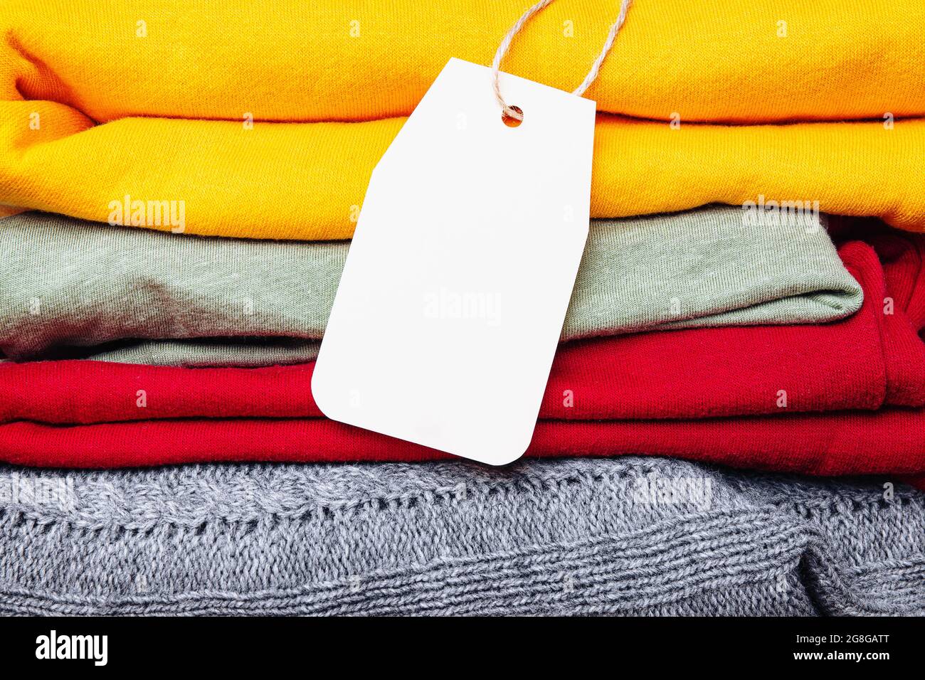 Vestiti in un palo, piegati in un mucchio di colori brillanti autunnali con un'etichetta vuota. Colori di tendenza del guardaroba autunnale. Spazio per il testo. Foto Stock
