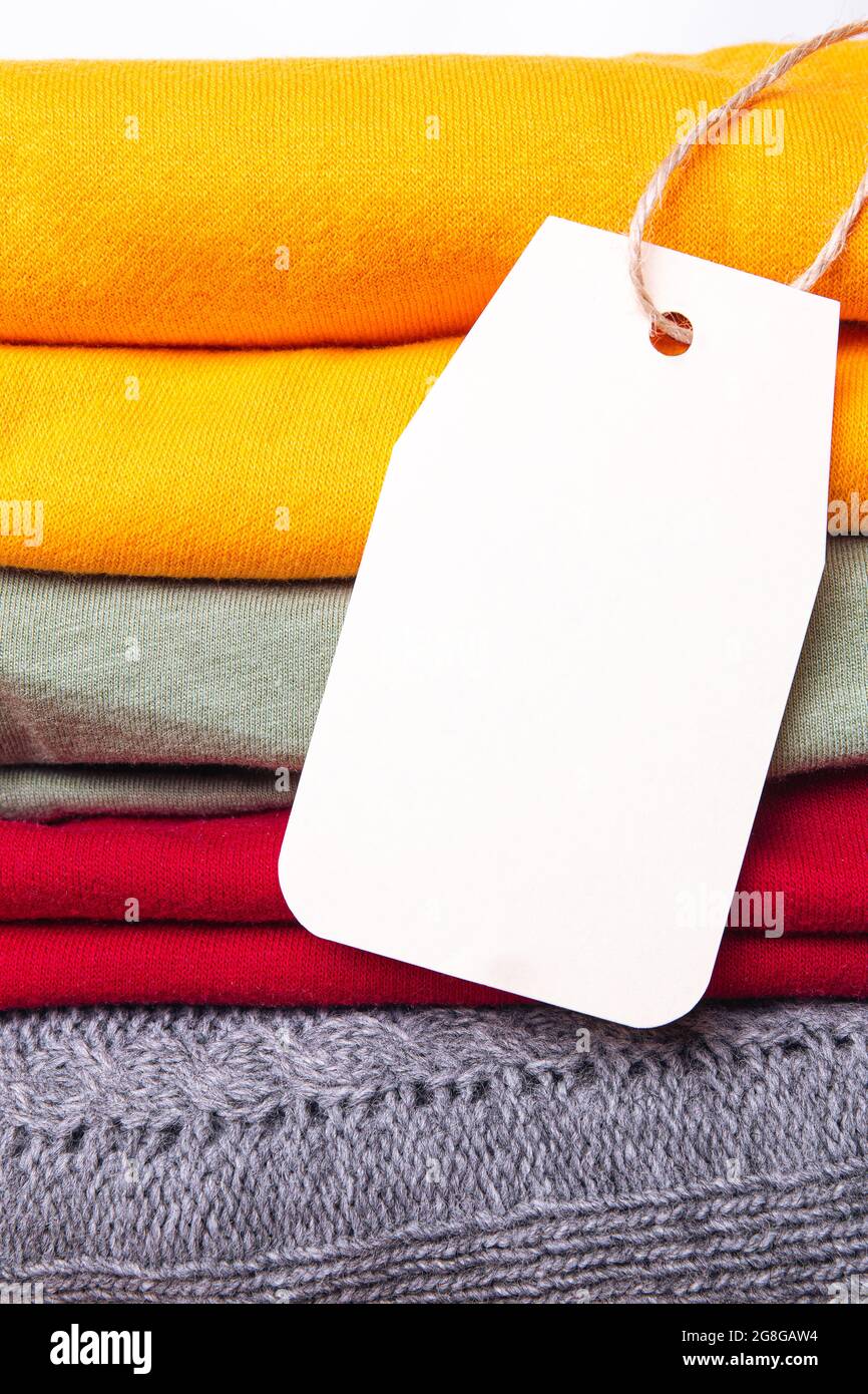 Vestiti in un palo, piegati in un mucchio di colori brillanti autunnali con un'etichetta vuota. Colori di tendenza del guardaroba autunnale. Spazio per il testo. Foto Stock