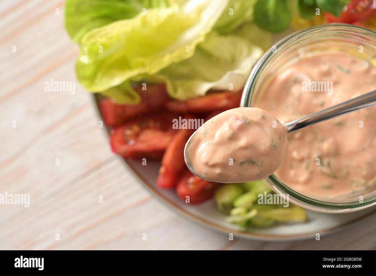 Salsa Thousand Island a base di skyr su un cucchiaio e in un vaso di vetro su fette di lattuga e insalata di pomodoro, sano pasto di cibo crudo, selezionato fuoco, molto Foto Stock