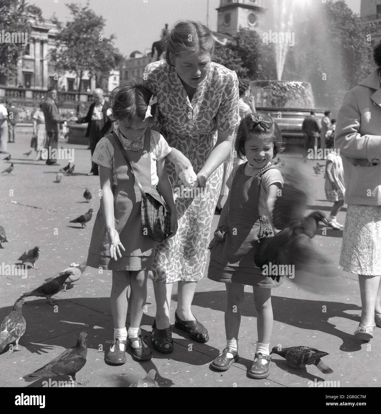 Anni '50, storico, una madre con le sue due giovani figlie, nutrendo i piccioni a Trafalgar Square, Londra, Inghilterra, Regno Unito. Un'attività tradizionale per oltre un centinaio di anni, greggi di piccioni scenderebbero sulla piazza per ricevere cibo da coloro che visitano il famoso punto di riferimento del centro di Londra. Foto Stock