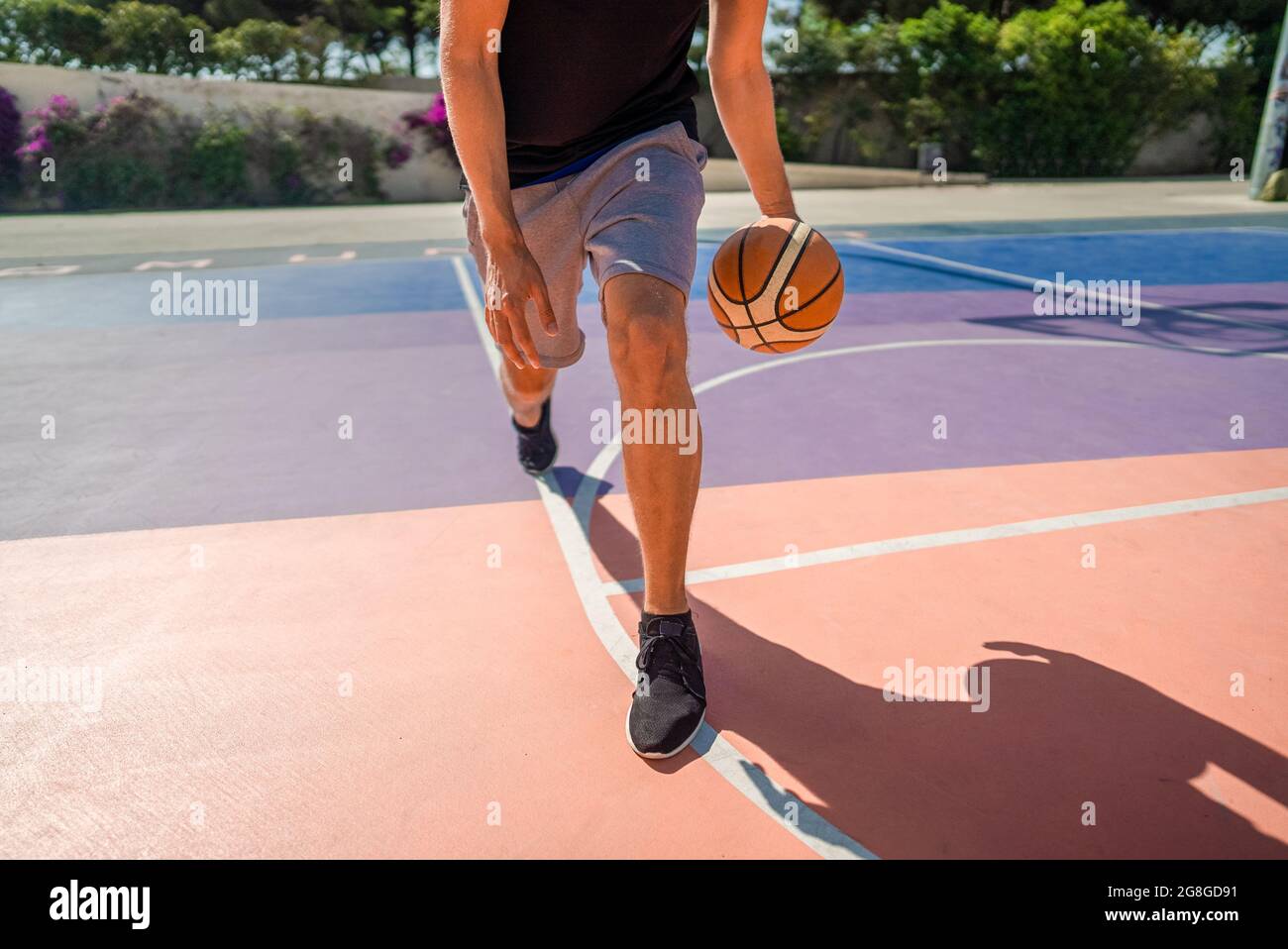 Gambe di un giocatore di basket professionista che dribbling la palla sul campo di pallacanestro. In estate durante il giorno caldo Foto Stock