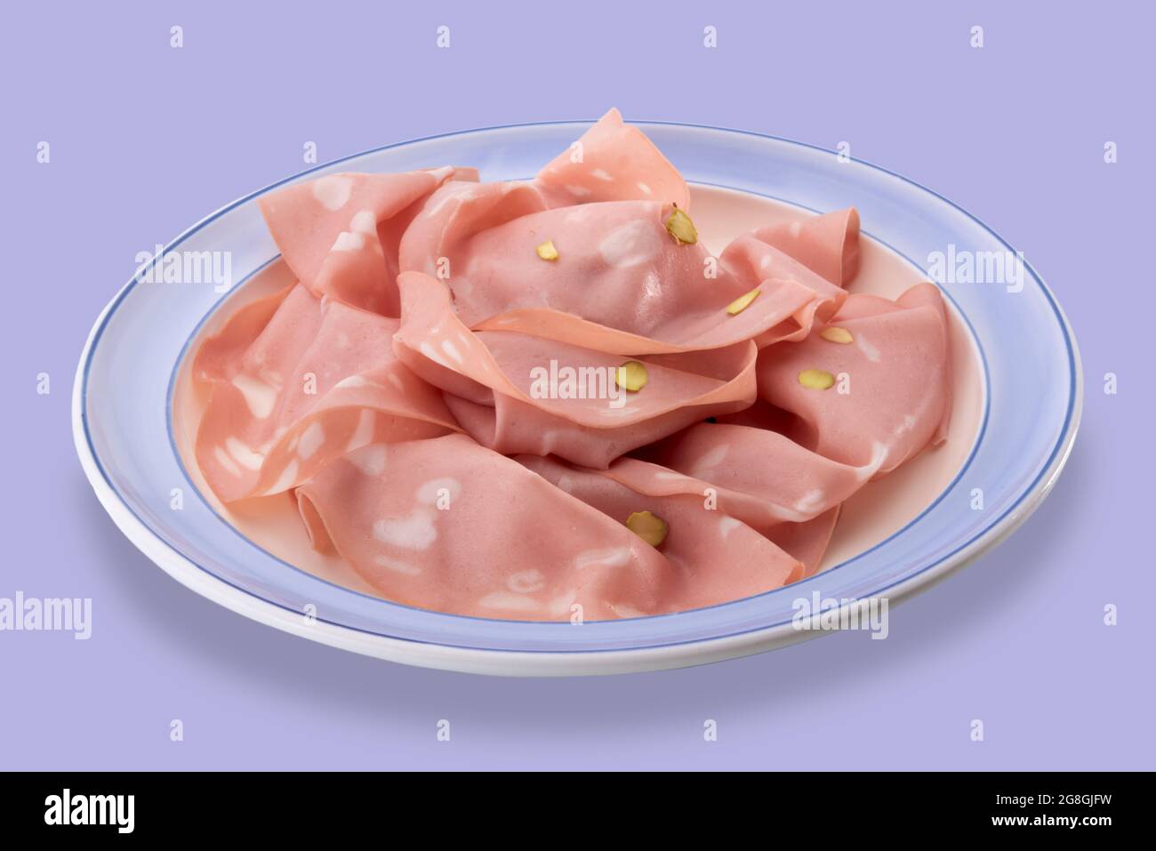 Mortadella bolognese con pistacchio, fette di salsiccia tipica italiana in piatto con bordo blu isolato su blu Foto Stock