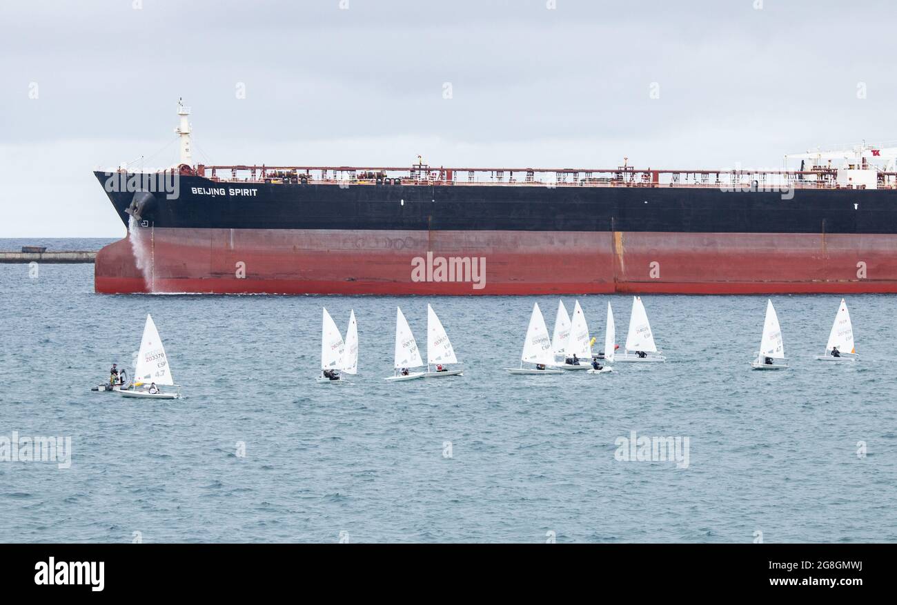 Piccole imbarcazioni a vela vicino a grandi petroliere. Foto Stock