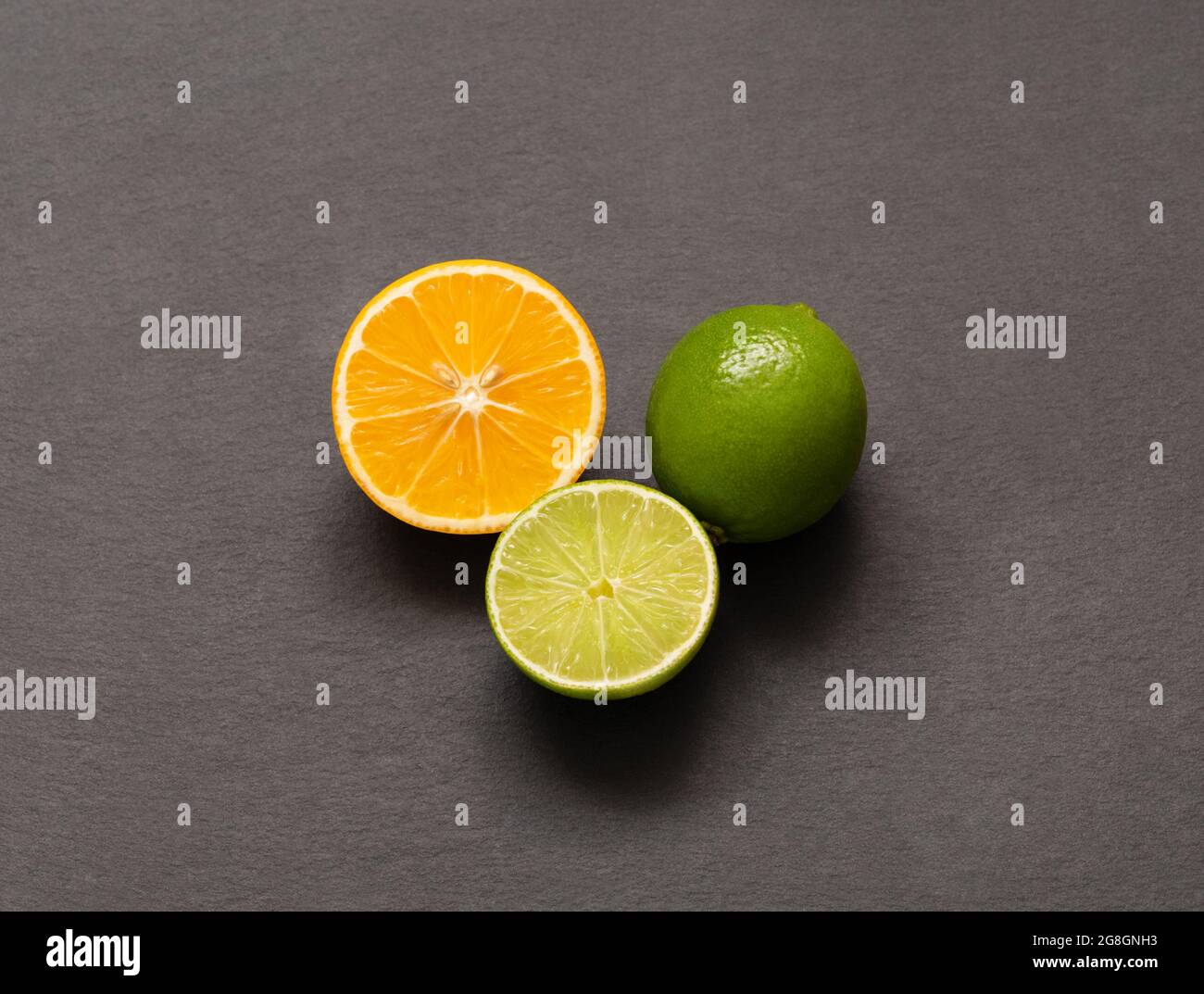 Limone di lime e arancio su sfondo grigio. Agrumi interi e affettato su un tavolo di pietra. Vista dall'alto, disposizione piatta. Foto Stock