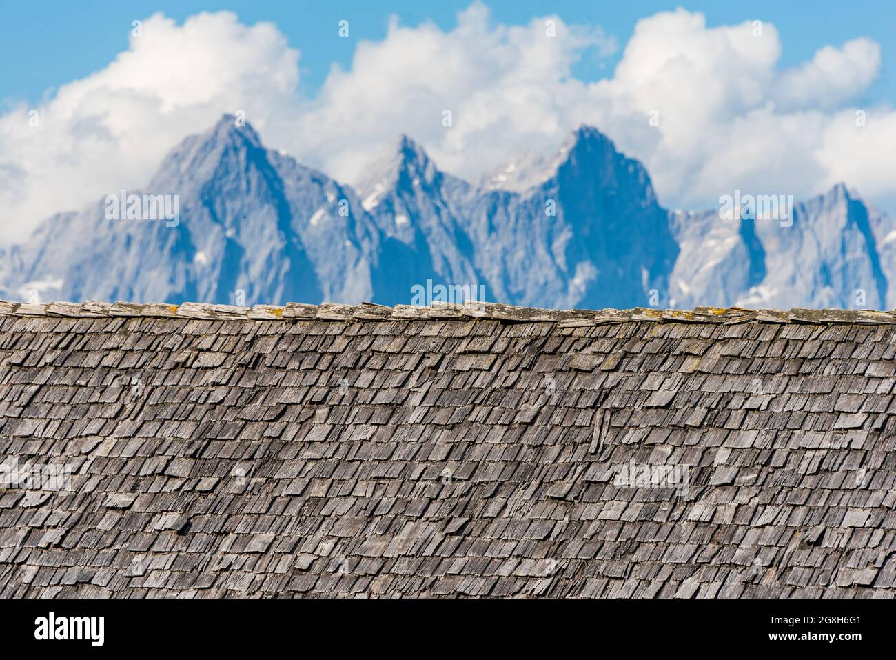 Intemperie e sbiadite dal sole, dalla pioggia e dalla neve, le frange di legno che sono il tetto di una casa alpina sullo sfondo di alte montagne alpine. WO Foto Stock