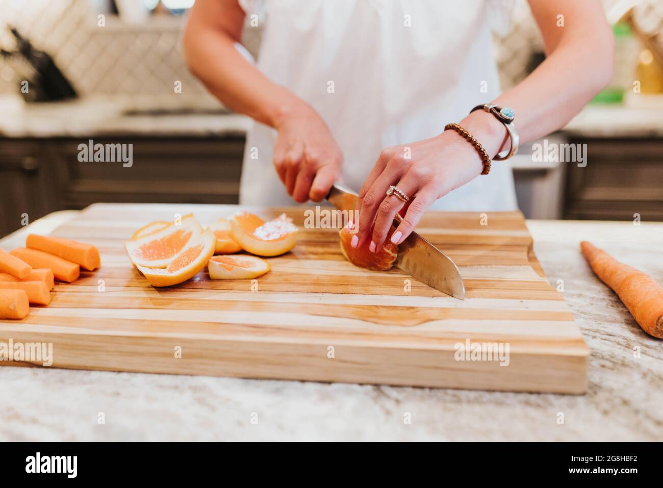 Primo piano di donna che taglia arance sul tagliere in cucina Foto Stock