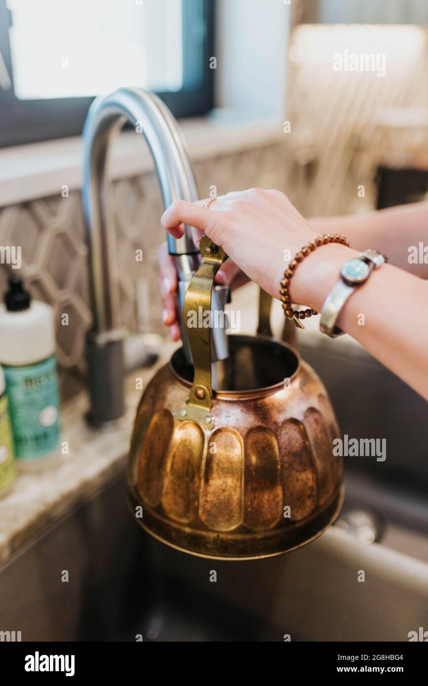 La donna fa funzionare l'acqua dal dispersore della cucina nel bollitore del tè di ottone per riscaldare Foto Stock