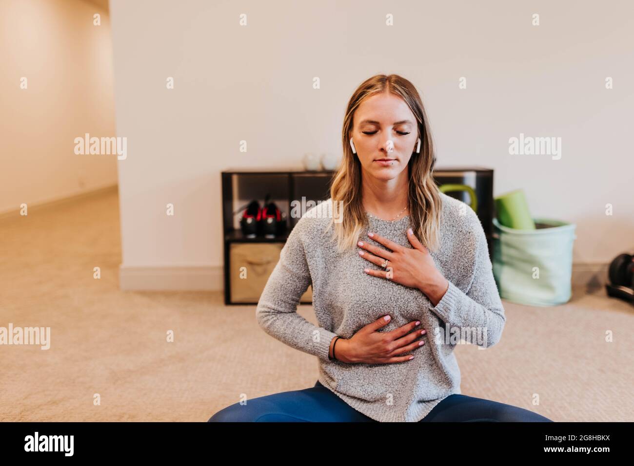 La donna indossa gli auricolari mentre medita nella sua palestra domestica Foto Stock
