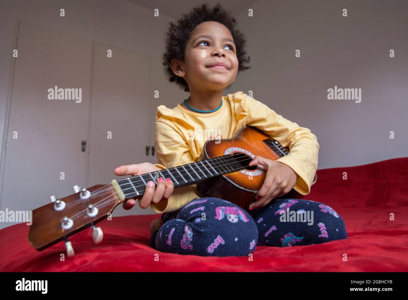 Bella ragazza gara mista che gioca a ukelele a casa Foto Stock