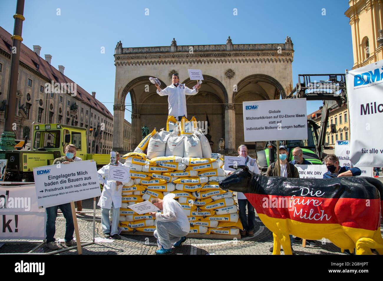 Demonstrant voller Geld, der die macht der Milch Konzerne symboliziert mit einem sarkastischen Schild: ' Billie Milch abholen & mit staatlichen Zuschuss einlagern. für uns vince! ' und wirft mit Geld um sich. Er steht auf 300 Säcke mit Milchpulver und Demonstranten mit Schilder und einer Milchkuh in Deutschlandfarben 'die faire Milch'. Am 18. Maggio 2020 haben zahlreiche Milchbauern für einen Milchpreis von mindest 40 cent demonstriert. Durch die Corona Krise ist Milchpreis Global deutlich gefallen und der BDM fordert einen staatlichen Eingriff. München, 18. Maggio 2020. (Foto di Alexander Pohl/ Foto Stock