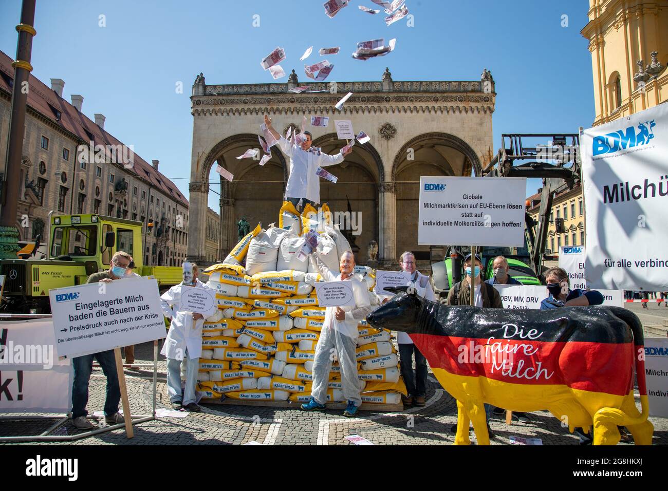 Demonstrant voller Geld, der die macht der Milch Konzerne symboliziert mit einem sarkastischen Schild: ' Billie Milch abholen & mit staatlichen Zuschuss einlagern. für uns vince! ' und wirft mit Geld um sich. Er steht auf 300 Säcke mit Milchpulver und Demonstranten mit Schilder und einer Milchkuh in Deutschlandfarben 'die faire Milch'. Am 18. Maggio 2020 haben zahlreiche Milchbauern für einen Milchpreis von mindest 40 cent demonstriert. Durch die Corona Krise ist Milchpreis Global deutlich gefallen und der BDM fordert einen staatlichen Eingriff. München, 18. Maggio 2020. (Foto di Alexander Pohl/ Foto Stock