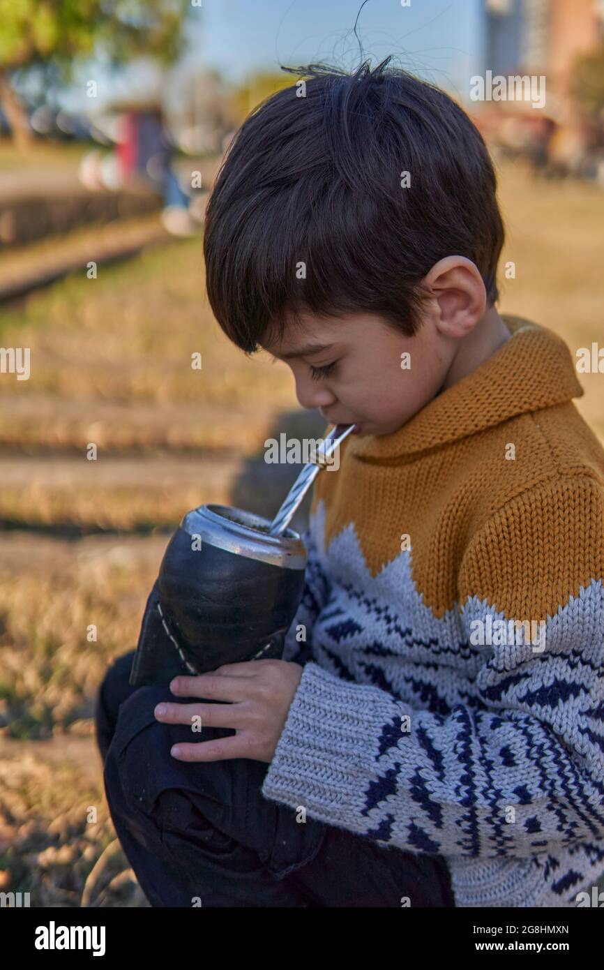 Ritratto di bambino brunette nel parco bevendo yerba mate presso le piste ferroviarie. Argentino personalizzato, verticale Foto Stock