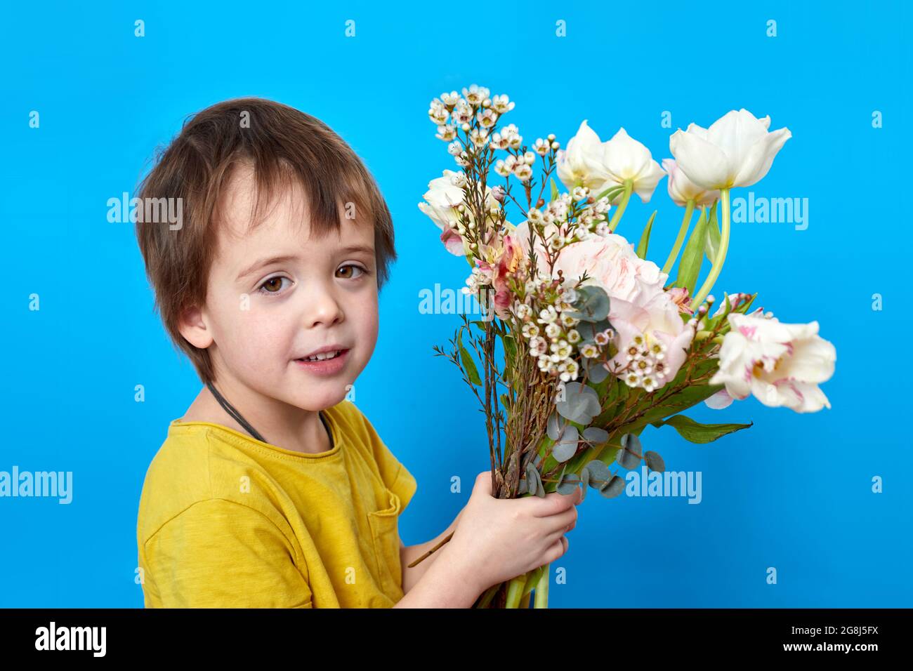 Vista laterale dell'adorabile bambino con bouquet di fiori in fiore con piacevole odore guardando la macchina fotografica Foto Stock