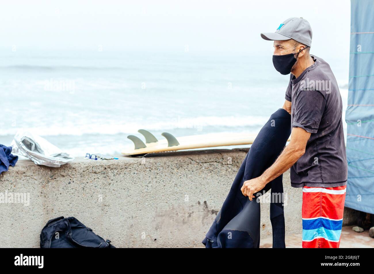 Uomo surfista più anziano con maschera protettiva covid-19 e una tavola da surf Foto Stock