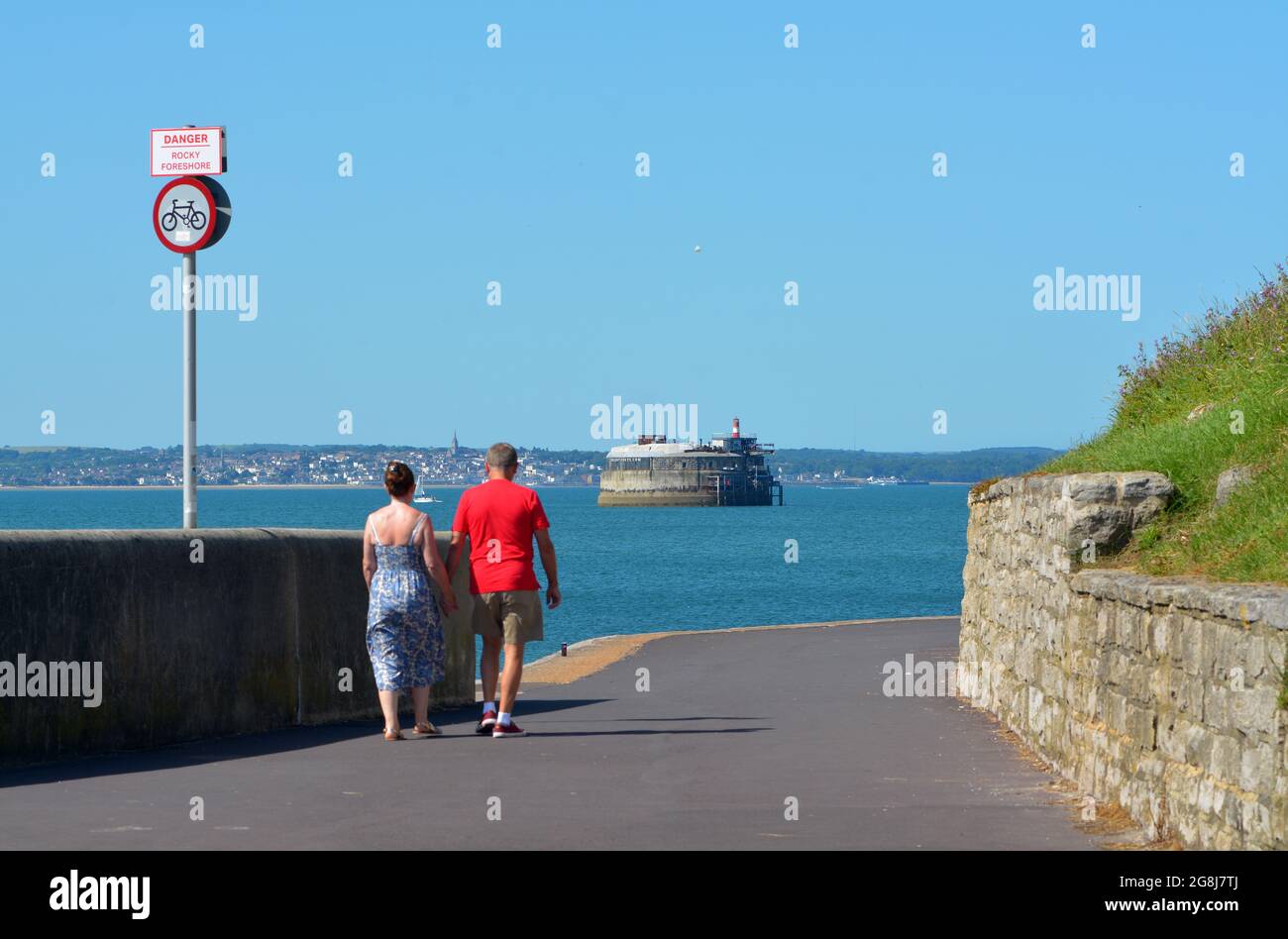 Un paio di persone camminano lungo il lungomare di Southsea, questa parte si curva intorno permettendo una vista fuori al forte di Spitbank e l'Isola di White. Foto Stock