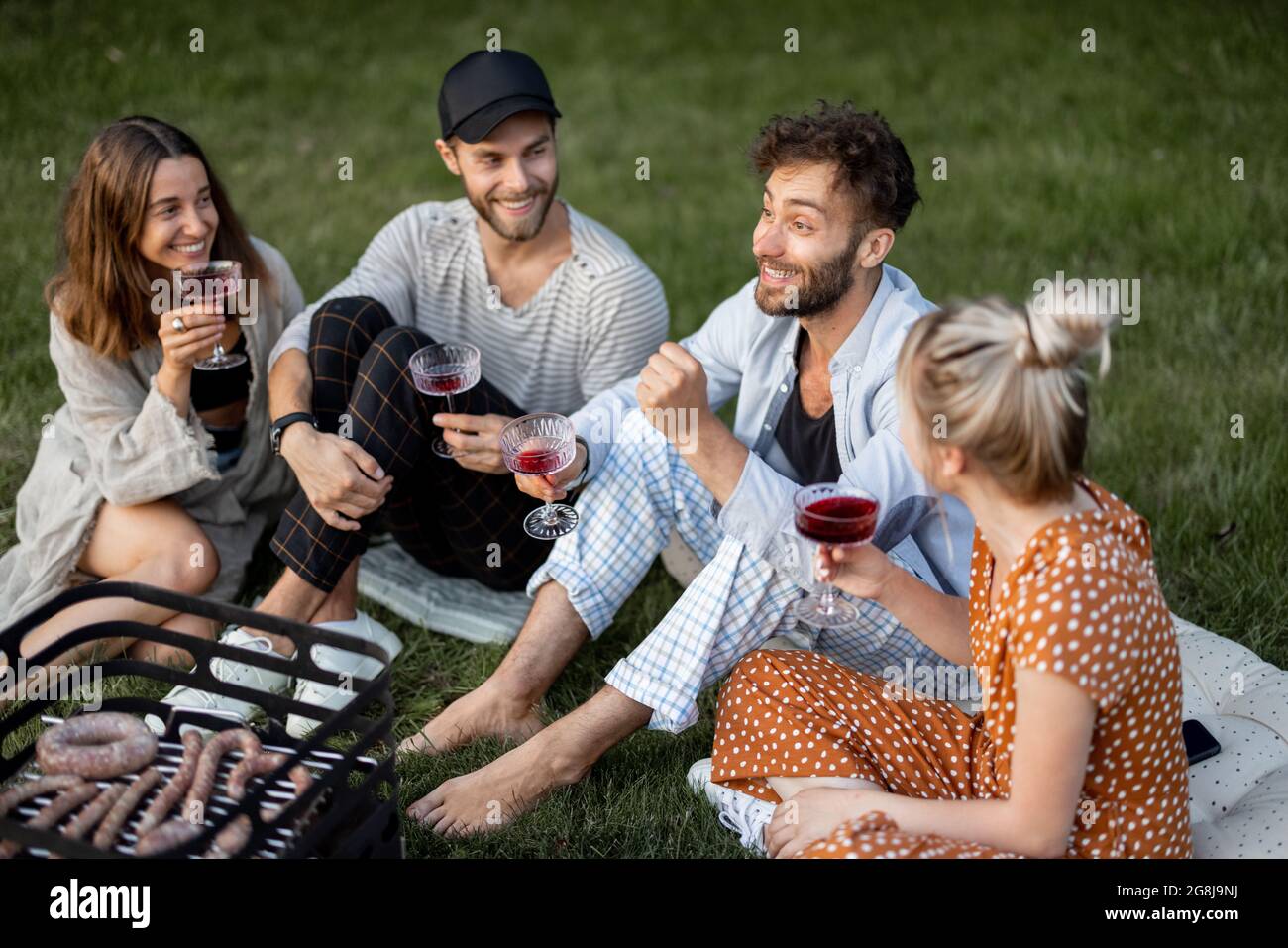 Amici seduti insieme al picnic con barbecue e vino Foto Stock