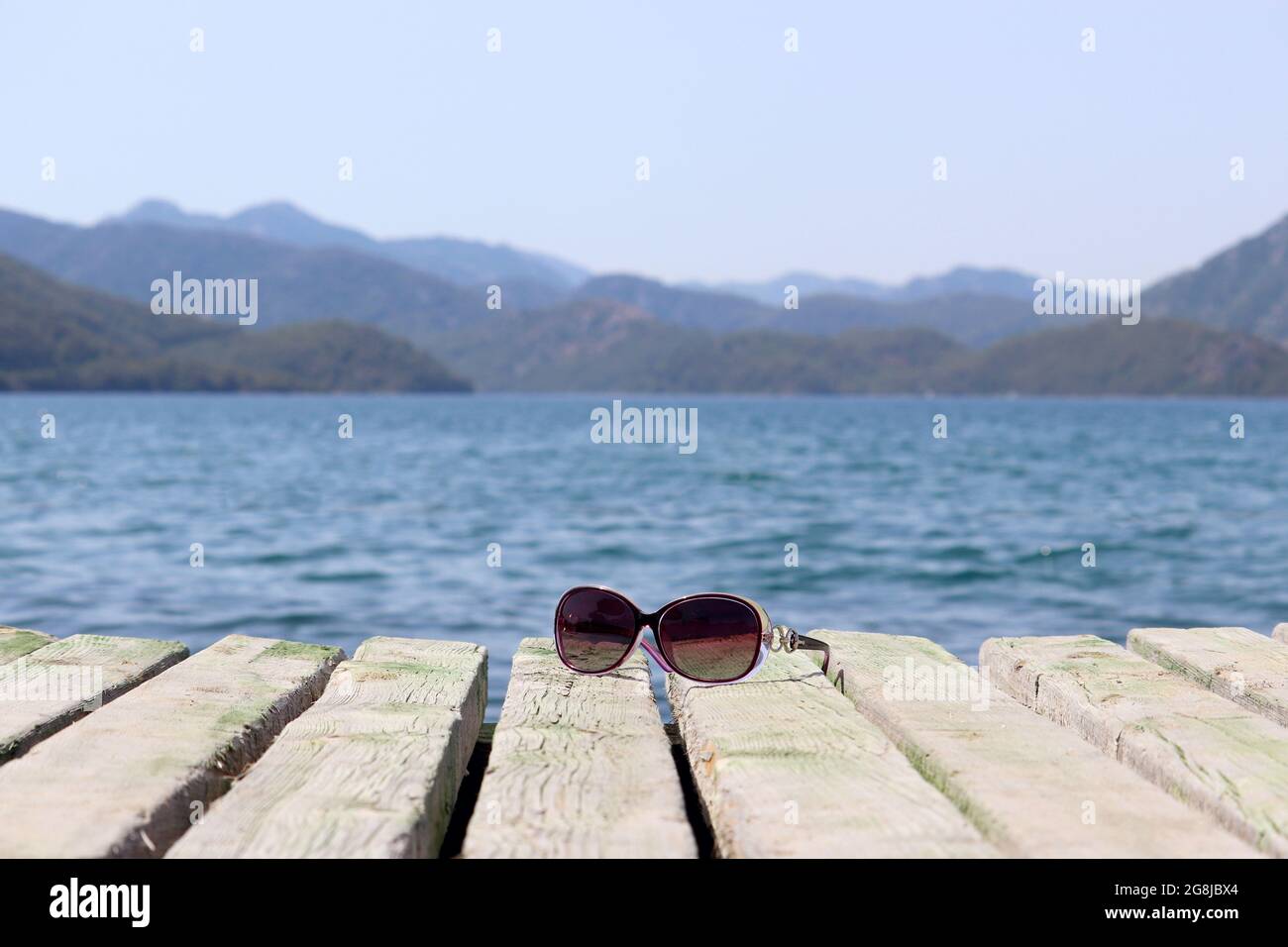 Occhiali da sole su un vecchio molo di legno sul mare e sullo sfondo di montagne nebbie. Vacanze estive e nuoto in spiaggia Foto Stock