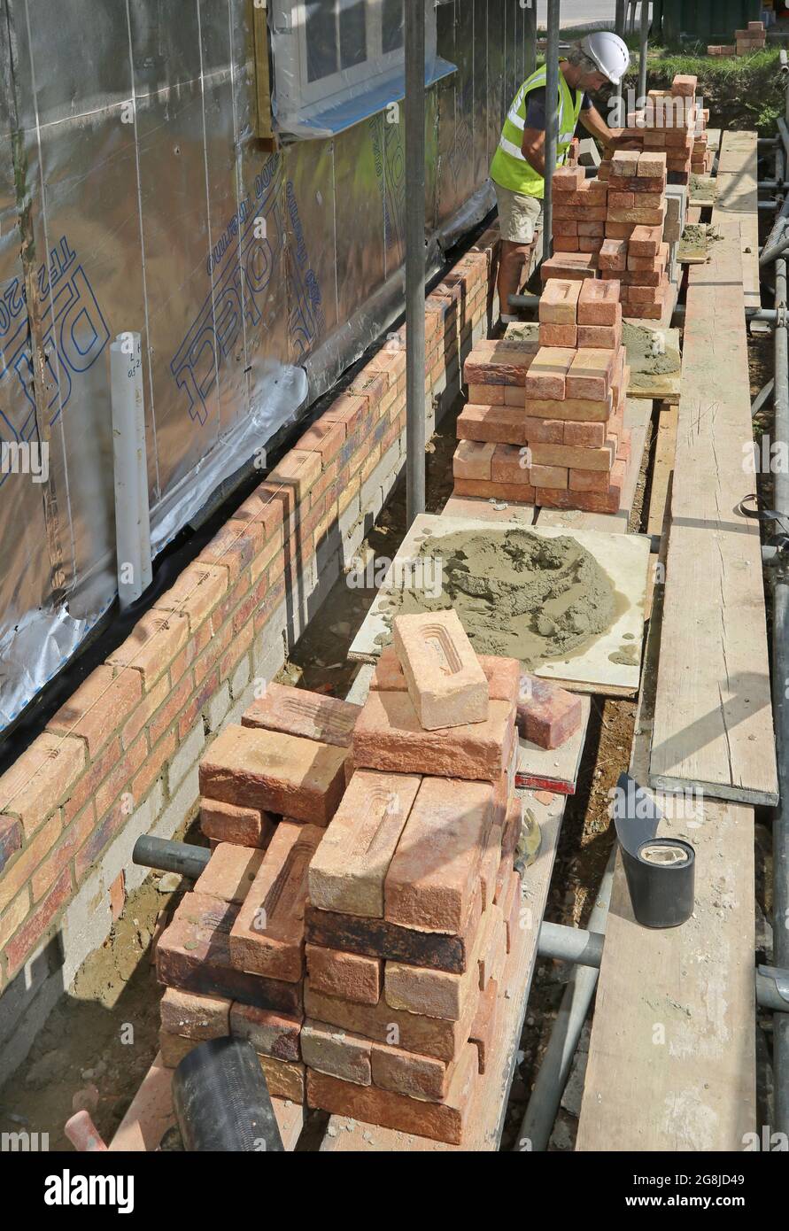 Uno strato di mattoni costruisce la parete esterna di un nuovo bungalow a Surrey, Regno Unito. Mostra impalcature caricate con tradizionali mattoni di argilla. Foto Stock