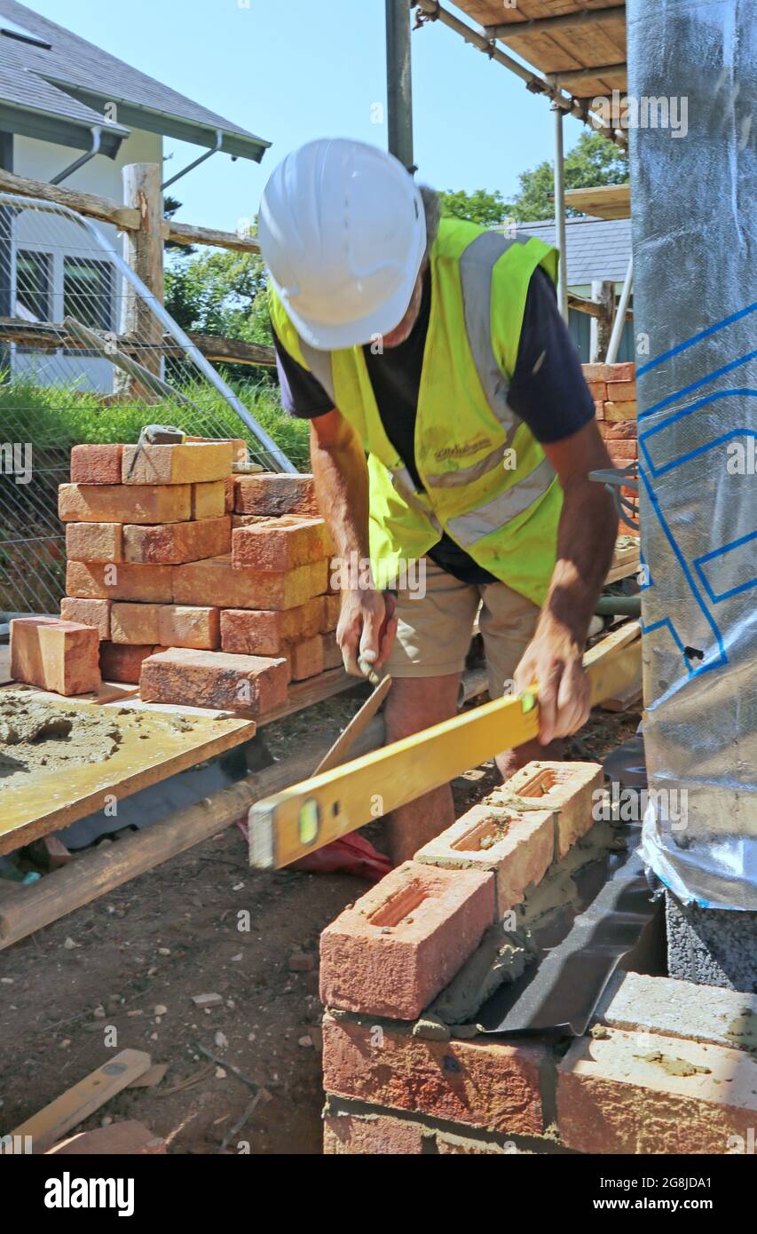 Uno strato di mattoni costruisce la parete esterna di un nuovo bungalow a Surrey, Regno Unito. Mostra impalcature caricate con tradizionali mattoni di argilla. Foto Stock