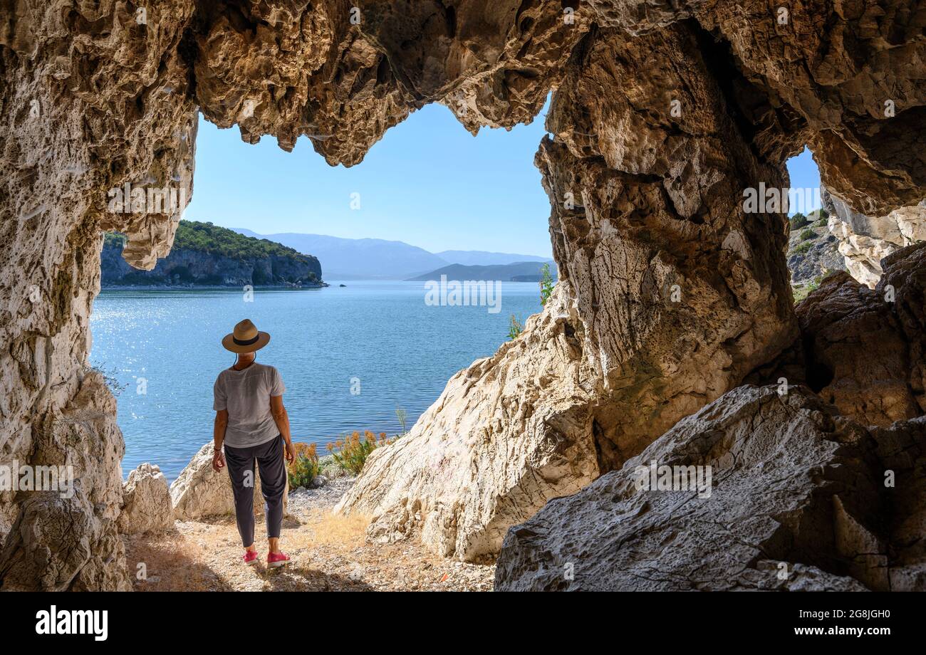 Un camminatore guarda attraverso il lago Prespa verso l'Albania da una grotta sulla riva vicino al villaggio di Psarades, in Macedonia, Grecia settentrionale. Foto Stock