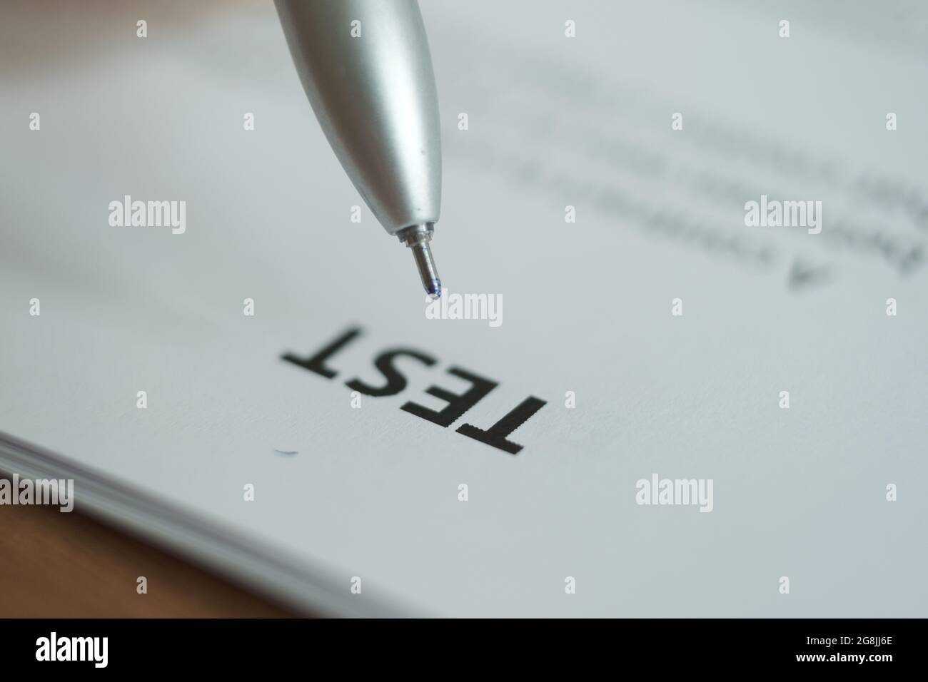 The word "Test" is written on a white sheet of paper, a pen is placed above the word. Blurred image. Foto Stock