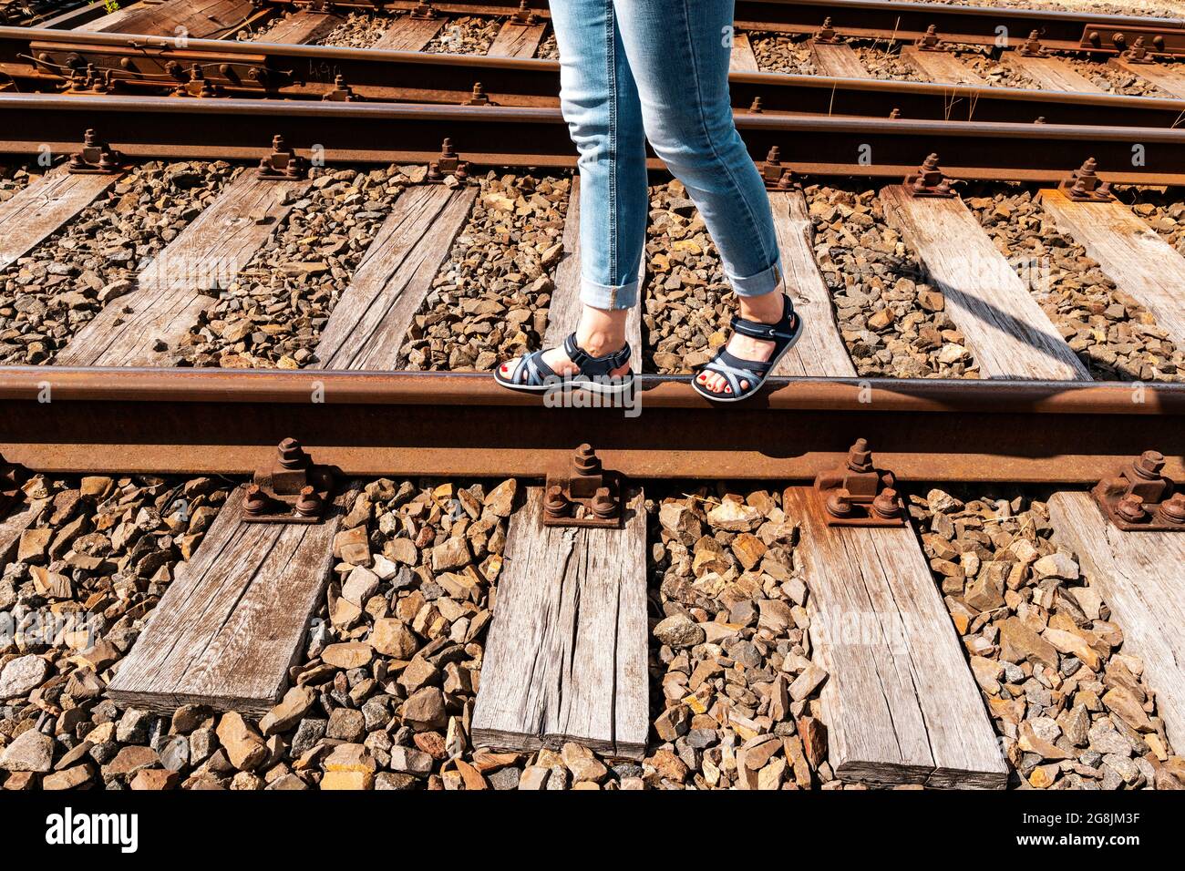 Donna che cammina sui binari del treno con sandali estivi. Concetto di viaggio. Foto Stock