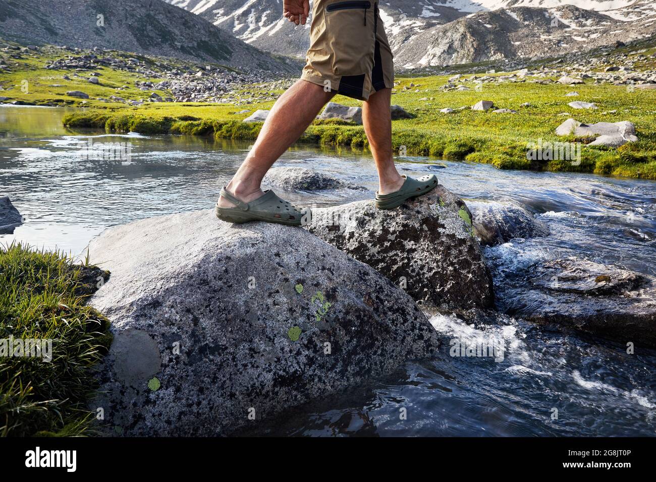 Uomo escursionistico che attraversa il fiume in scarpe verdi da pietre in equilibrio su caduto in Kazakistan Foto Stock