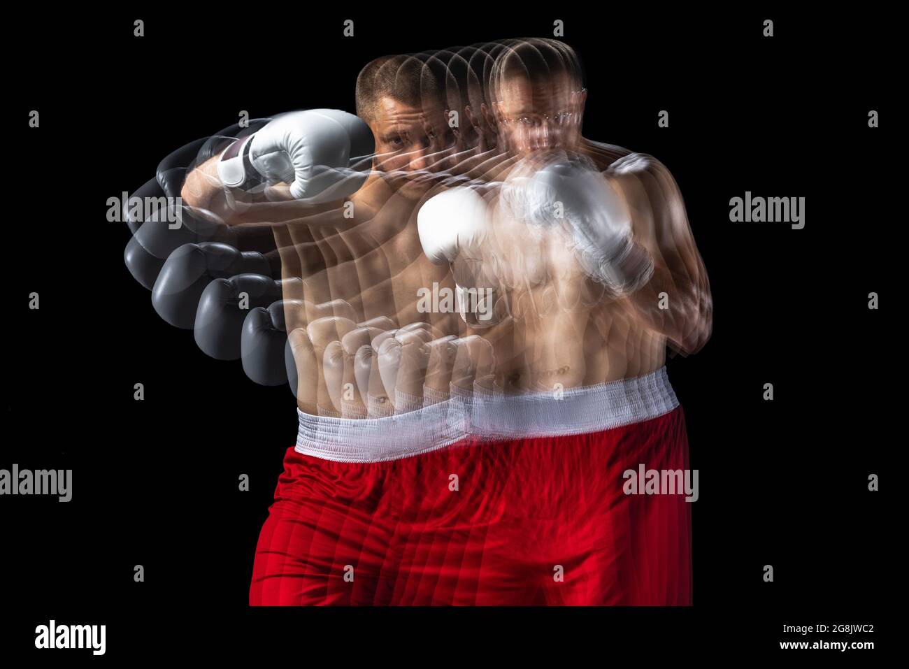 Giovane pugile professionista in shorts rosso allenamento, allenandosi su sfondo nero. Stroboscopio Foto Stock