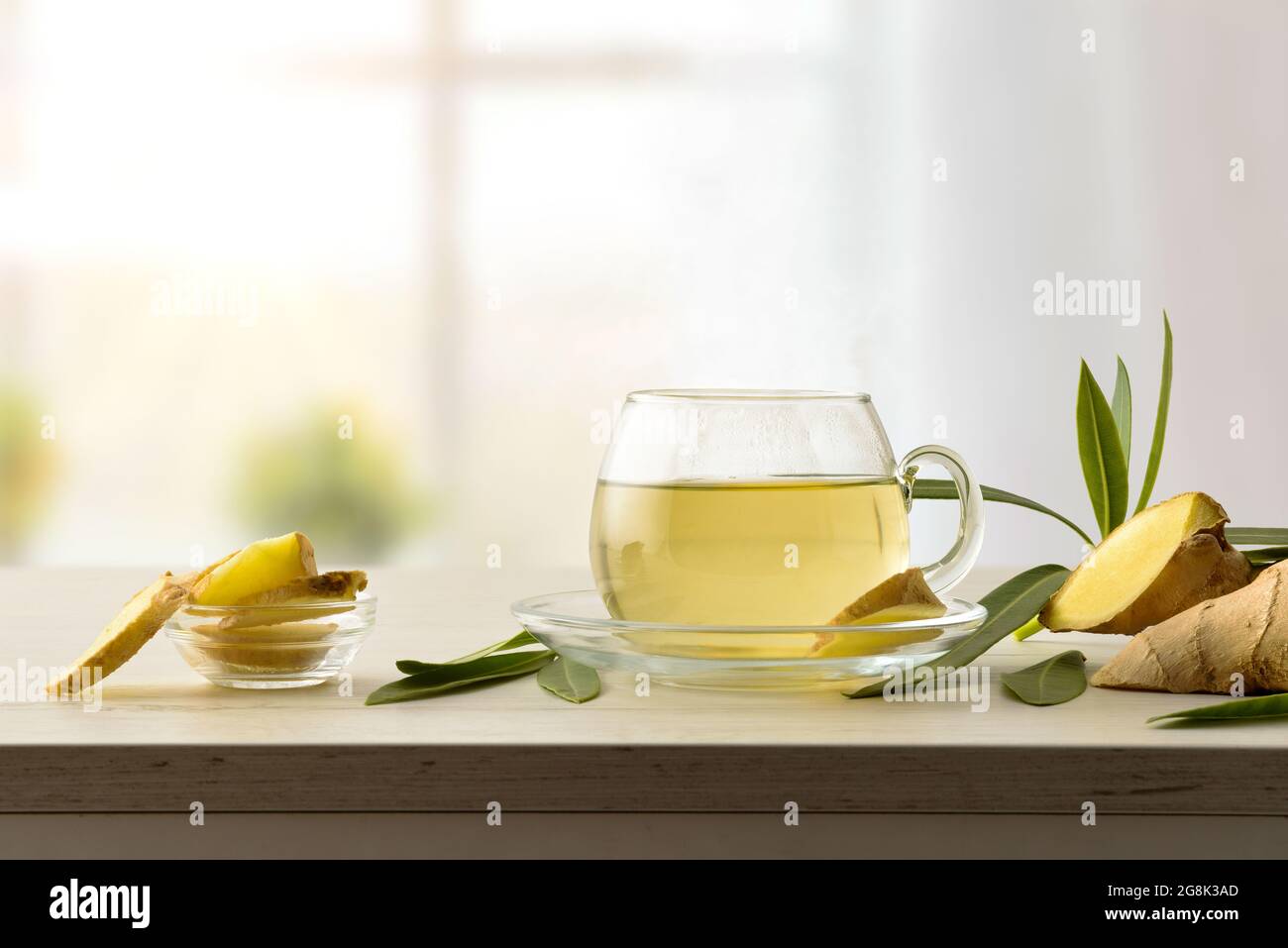Bicchiere di zenzero caldo su un tavolo di legno con radice di zenzero e foglie in soggiorno. Vista frontale. Foto Stock